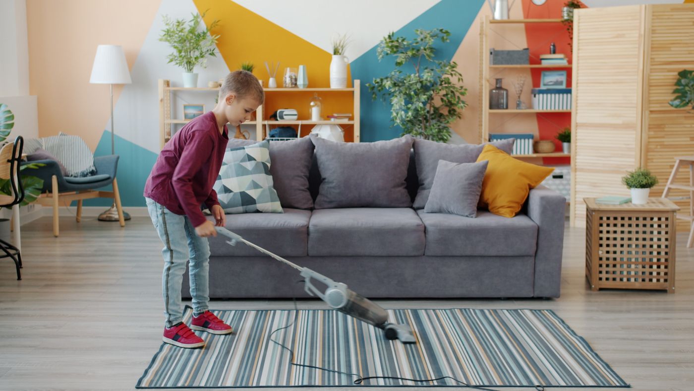 A child vacuuming a striped rug in a bright living room